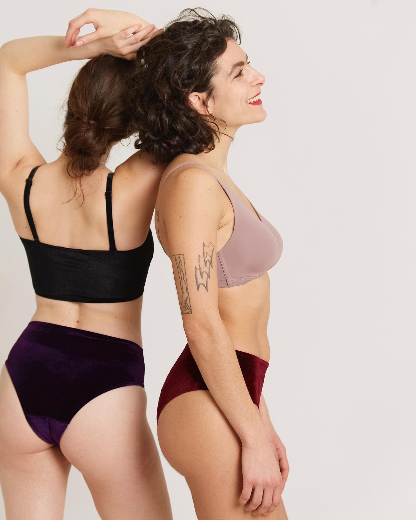 Two models in bras and high-waisted briefs, one in black and plum, one in mauve and burgundy.
